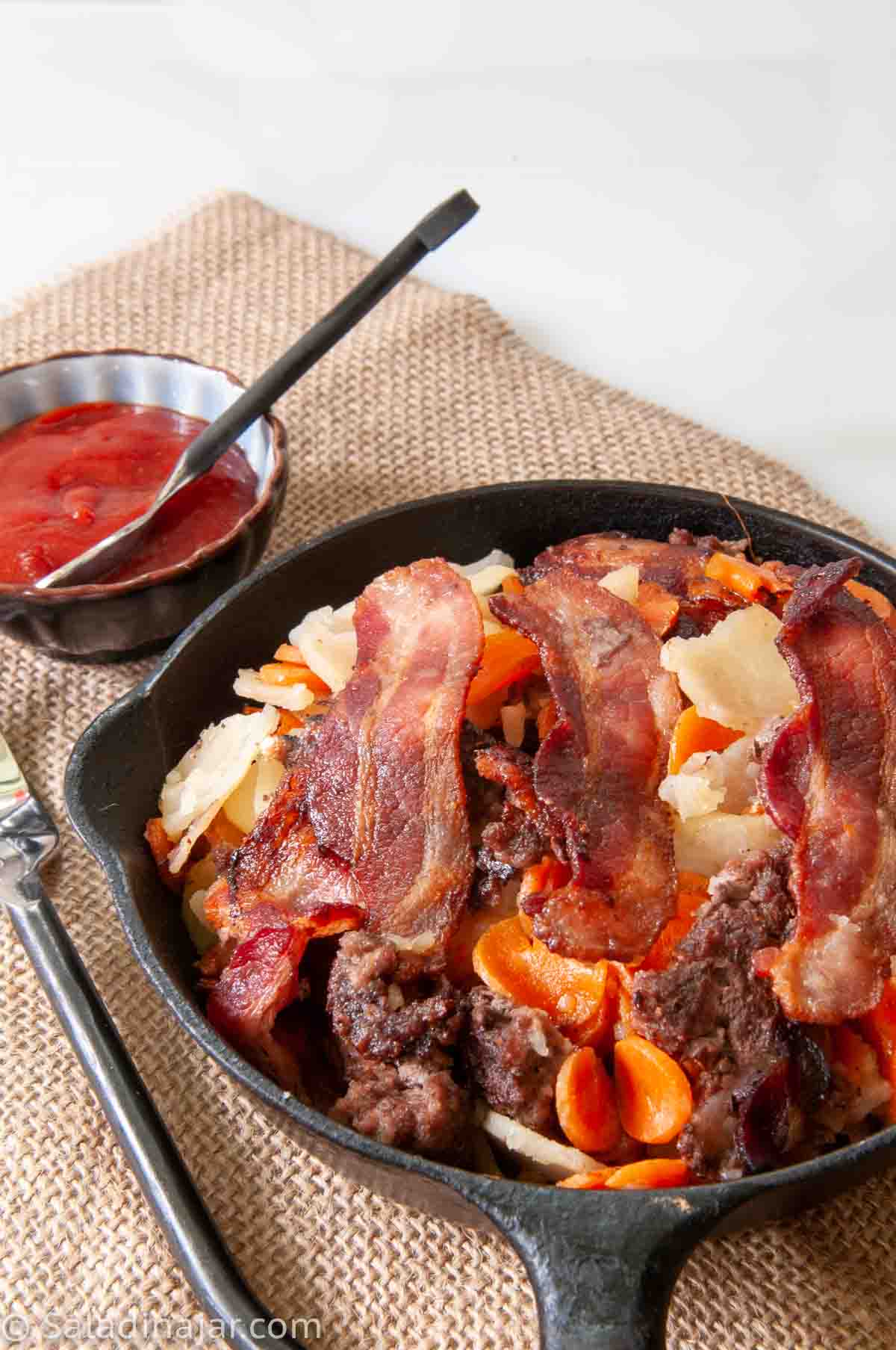 picture of Ground Beef and Potatoes Skillet with Bacon in a black iron skillet with catsup on the side.