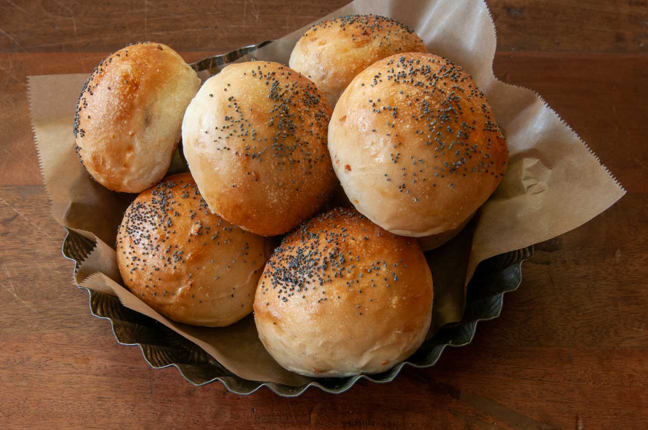 Sourdough rolls with toasted onion and poppy seeds on top in a metal basket