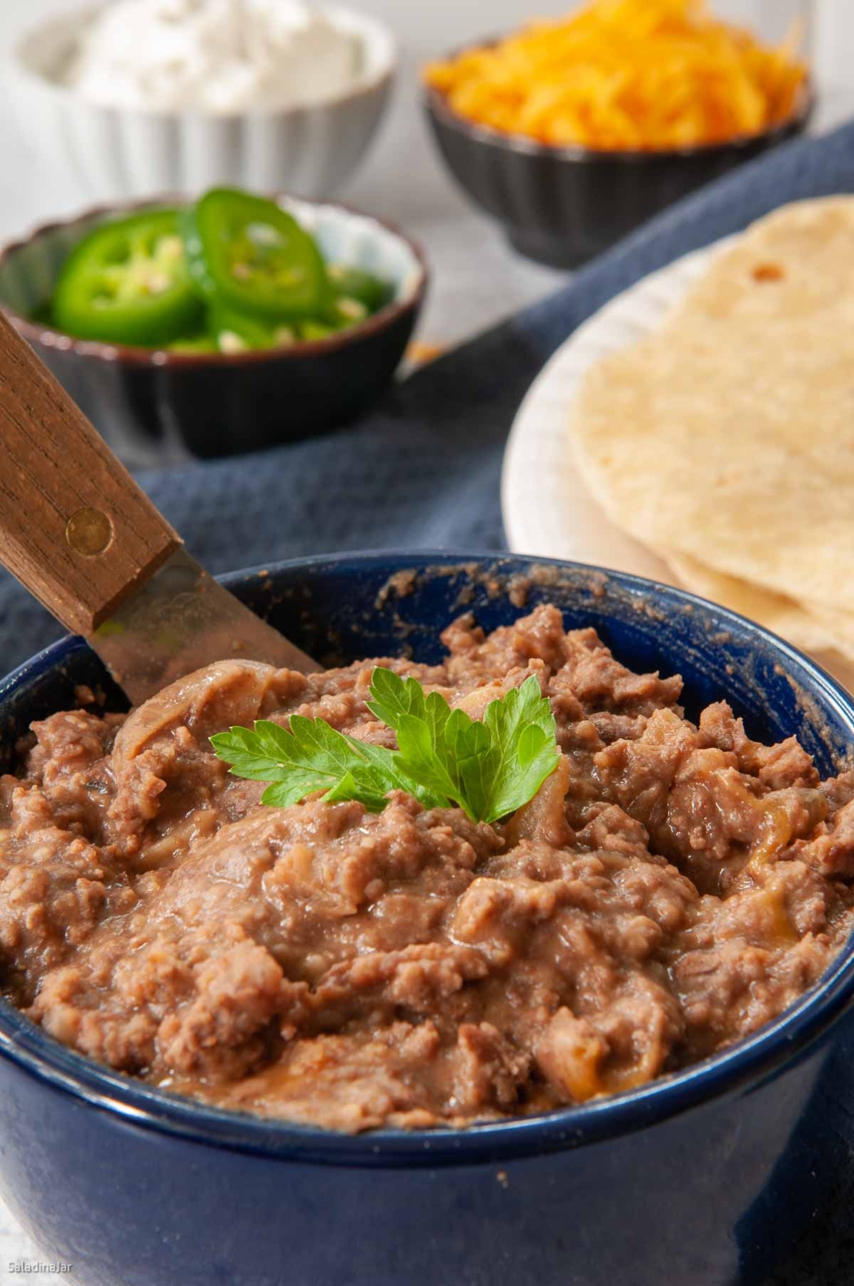 refried beans in a bowl with tortillas, jalapenos, cheese and sour cream