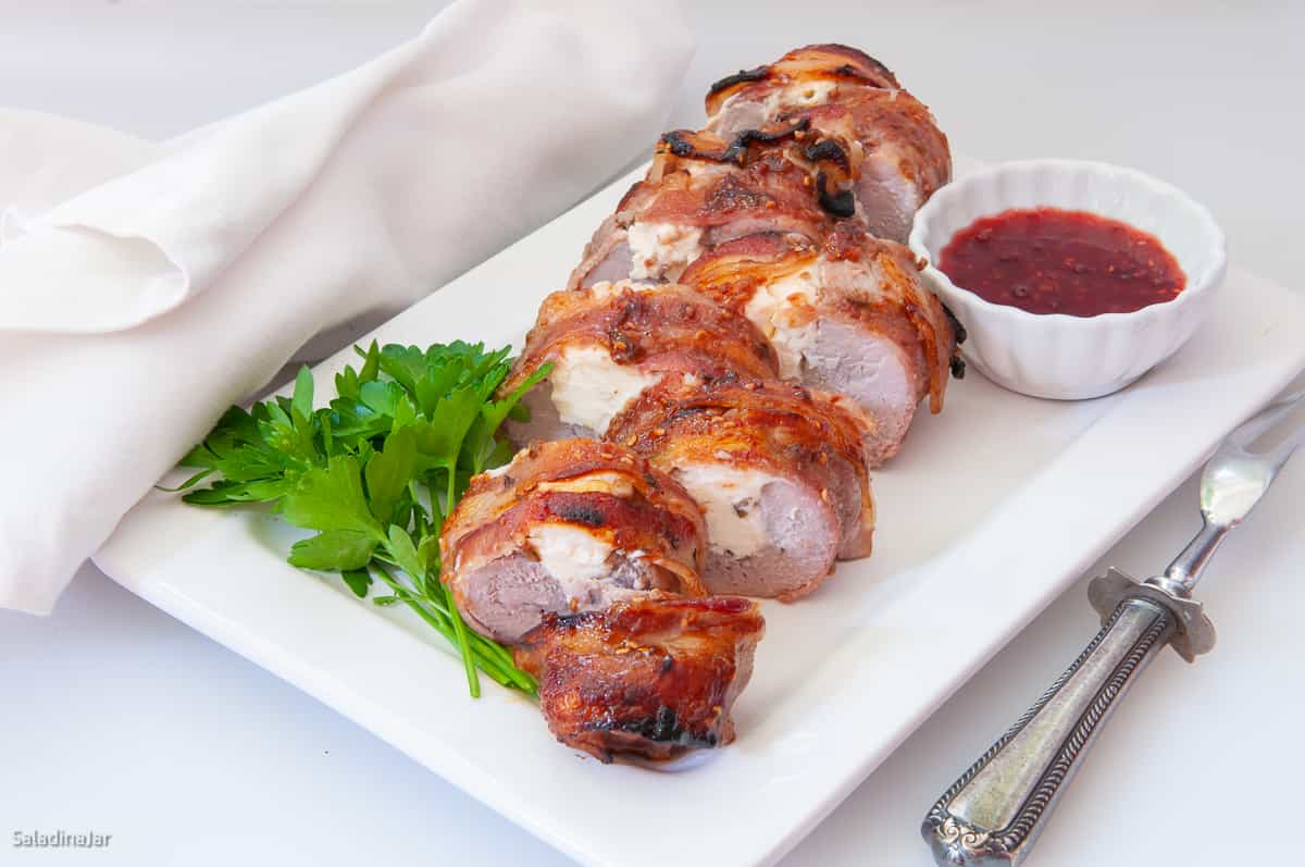 sliced bacon-wrapped pork tenderloin with raspberry sauce on the side