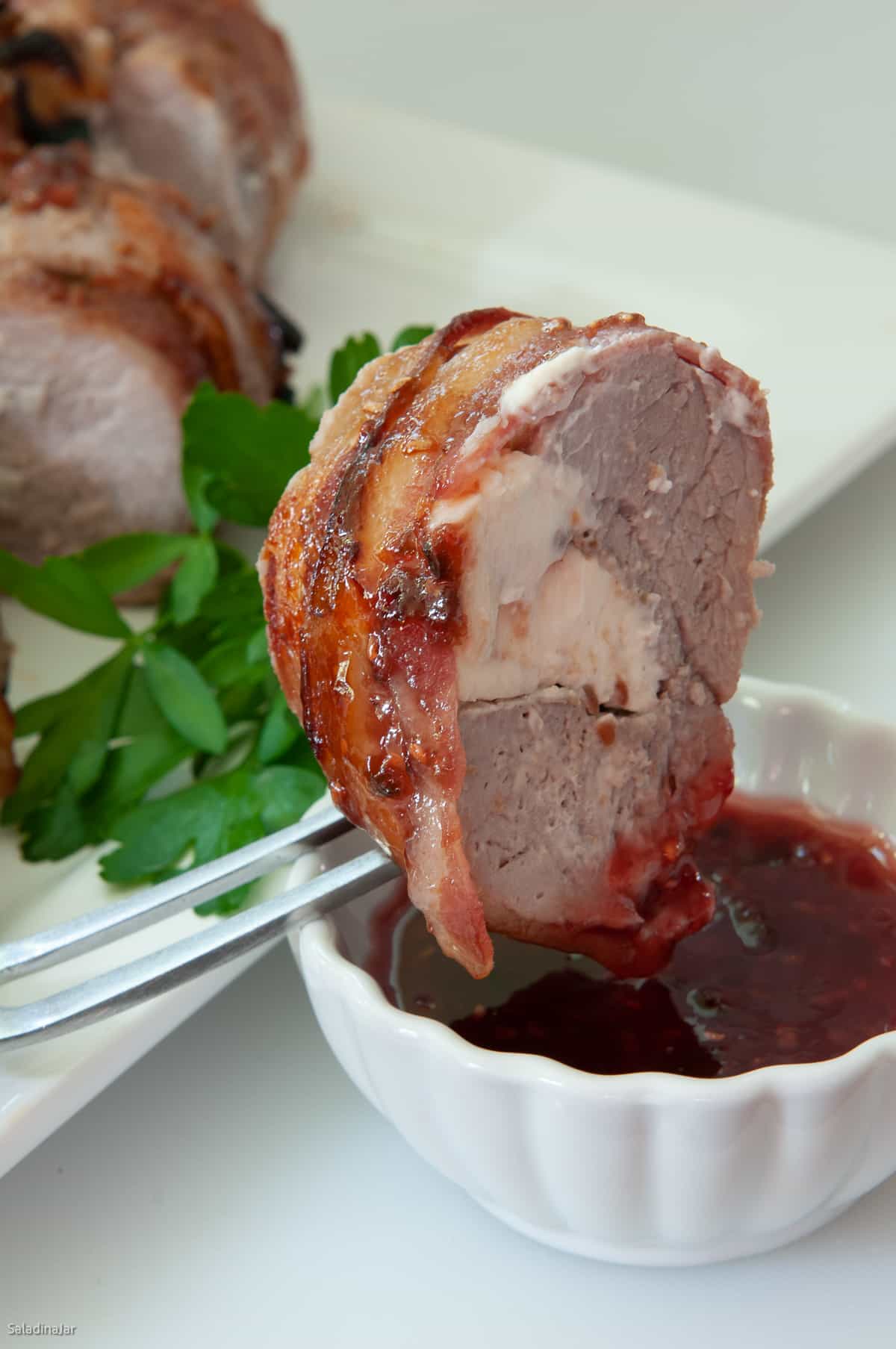 slice of wrapped tenderloin being dipped in sauce