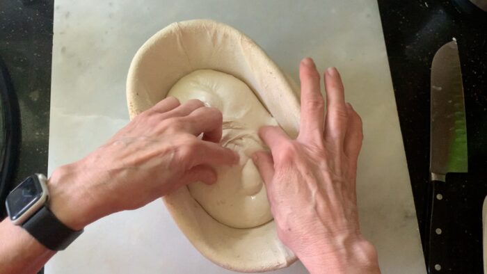 placing the dough upside down into a lined basket before carefully stitching the dough to create more tension.