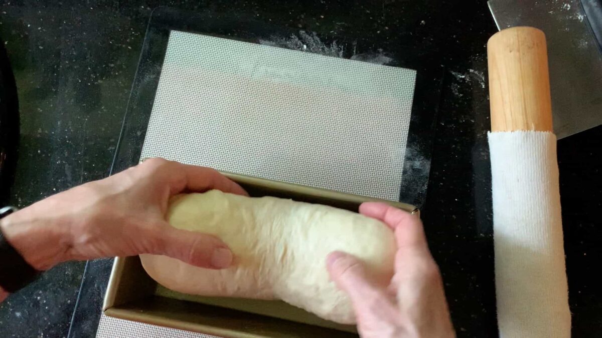 Dropping the bread into the pan seam-side down.