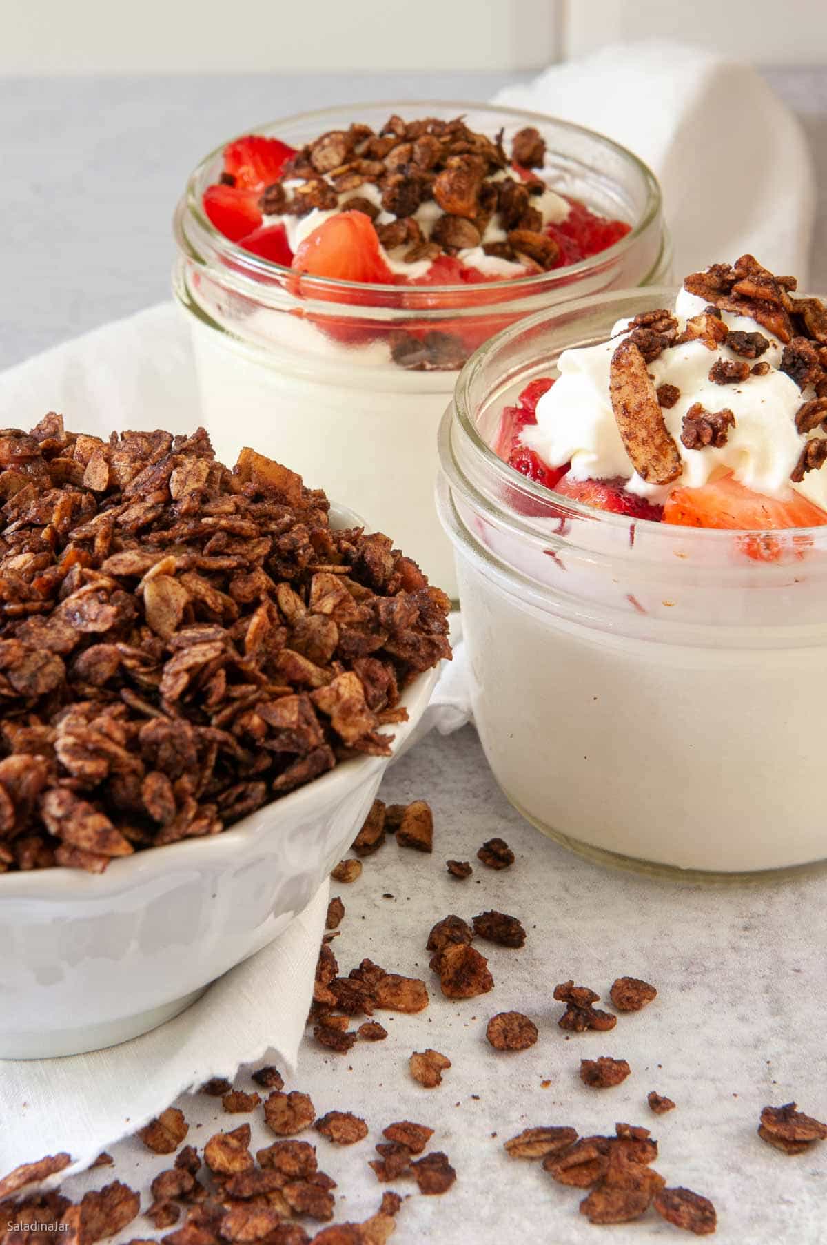 chocolate granola sprinkled over jars of fruit and yogurt.