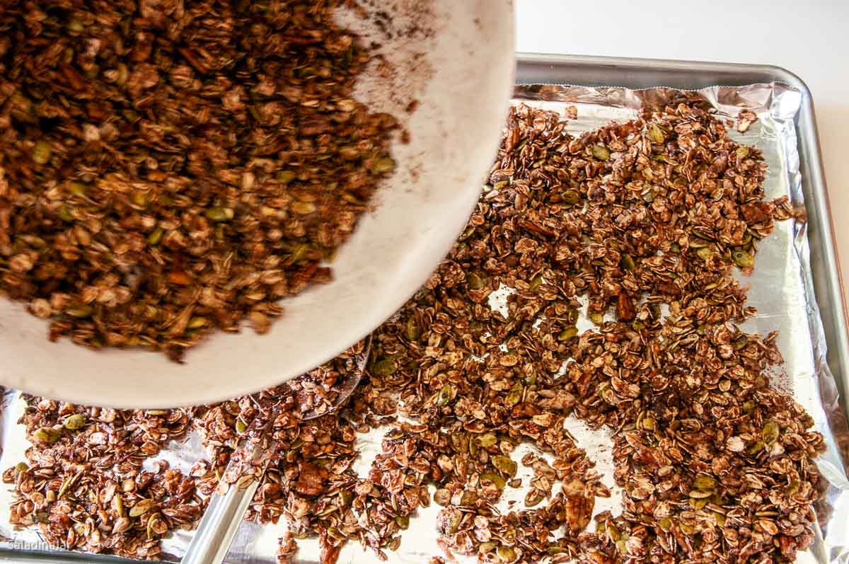 spreading granola on a cookie sheet