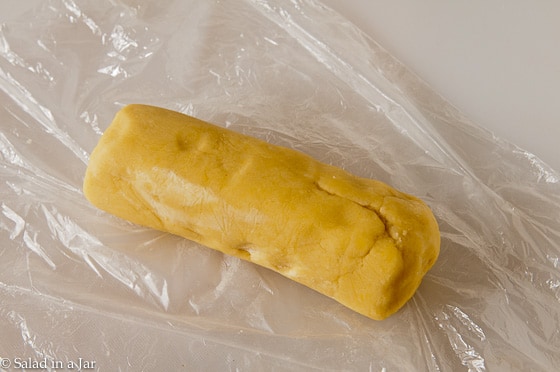 short bread dough shaped into a cylinder and wrapped in plastic wrap.