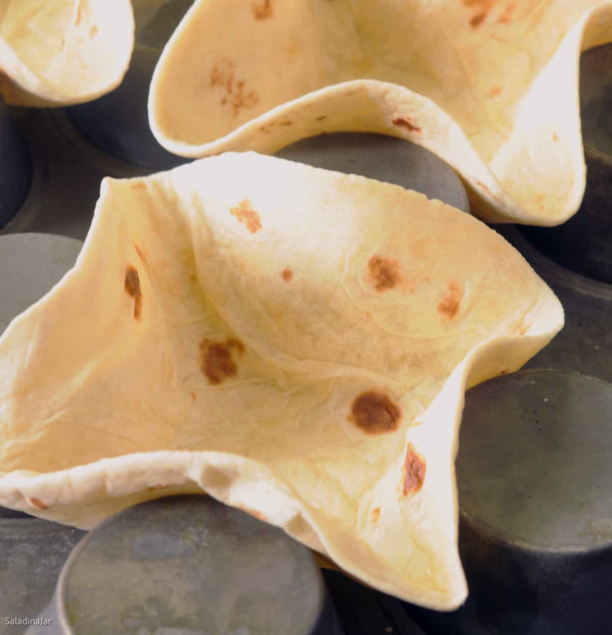 unbaked tortillas placed in upside down muffin tin