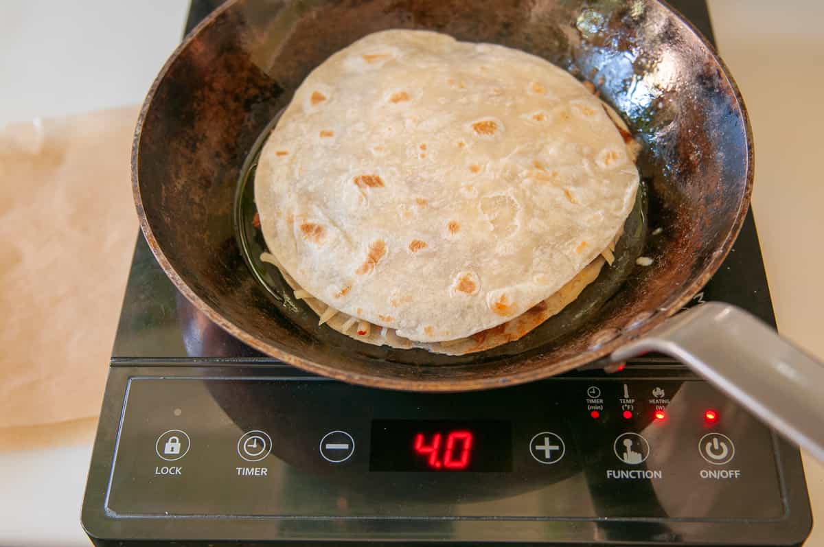 use the paper or plate you assemble the quesadilla on to transfer it to a hot skillet