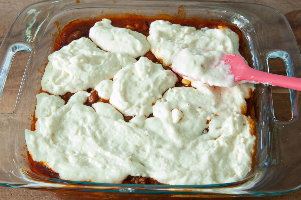 Spreading spoonfuls of the cornmeal mixture over the top of the meat layer.