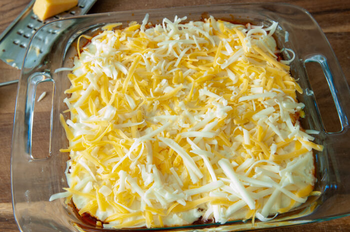 Adding cheese over the top of the cornmeal batter.