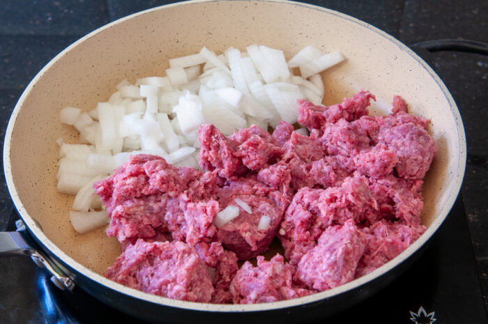 raw ground beef and onions in a skillet on the stove.
