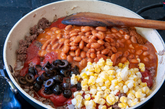 Tomato sauce, beans, corn, olives, and seasonings added to cooked meat.