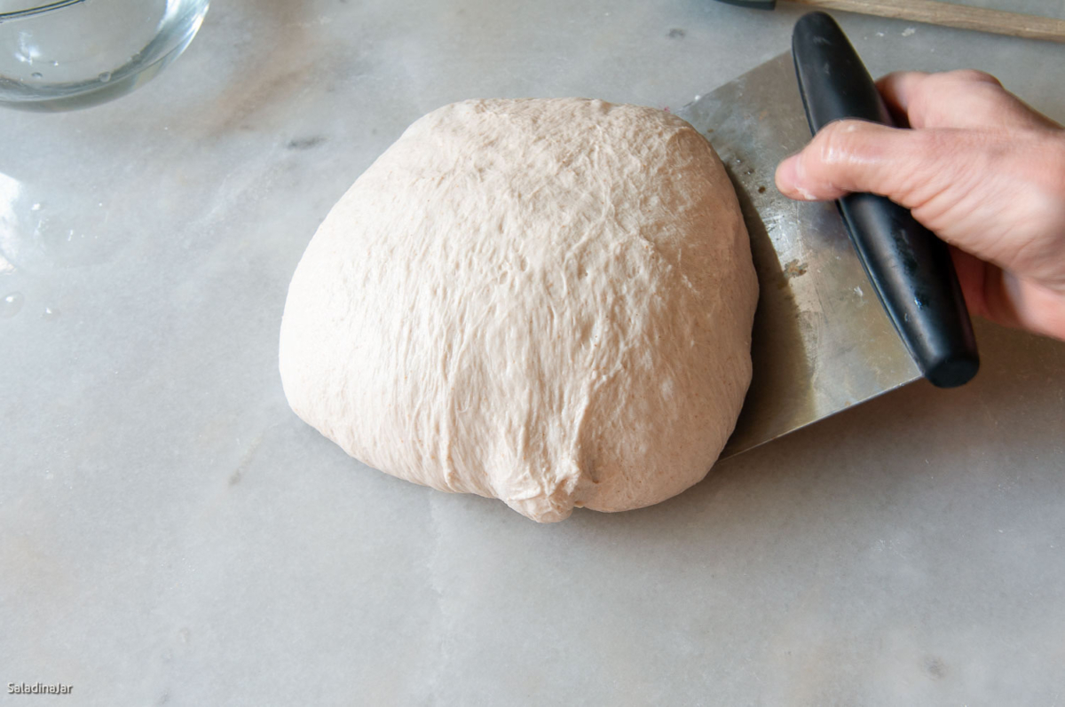 using a bench scraper to manipulate the dough to create tension