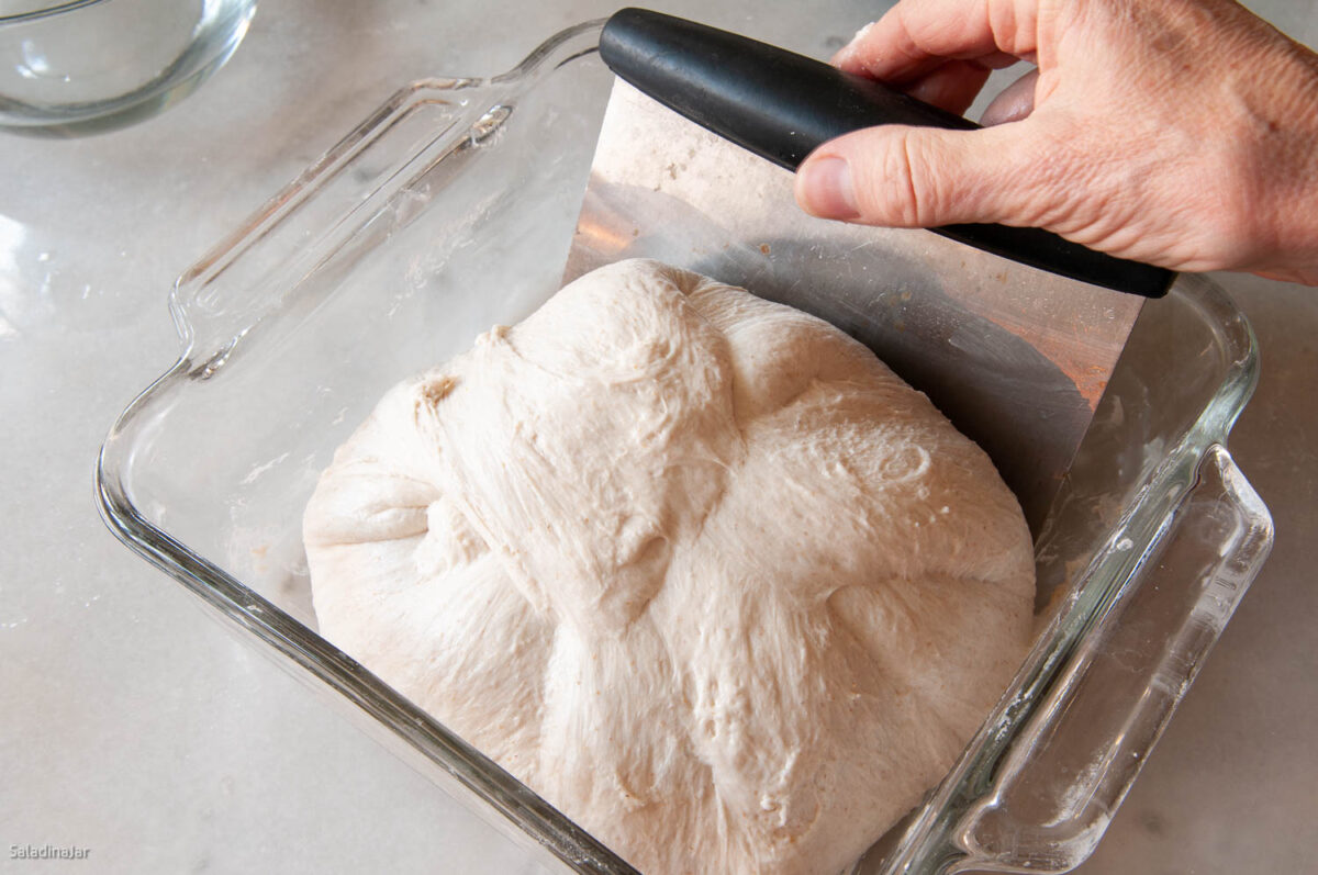 Using a bench scraper to remove the dough from the dish