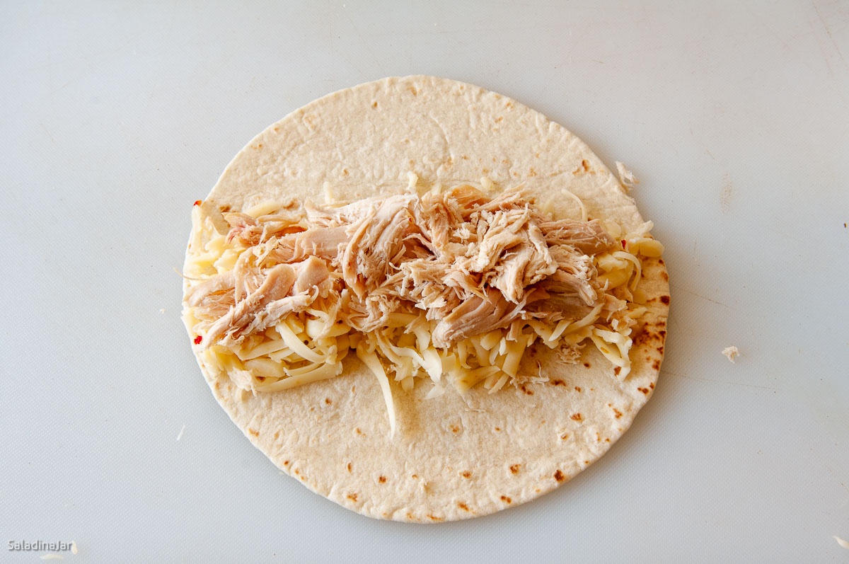 Assembling flautas: chicken on top of cheese.