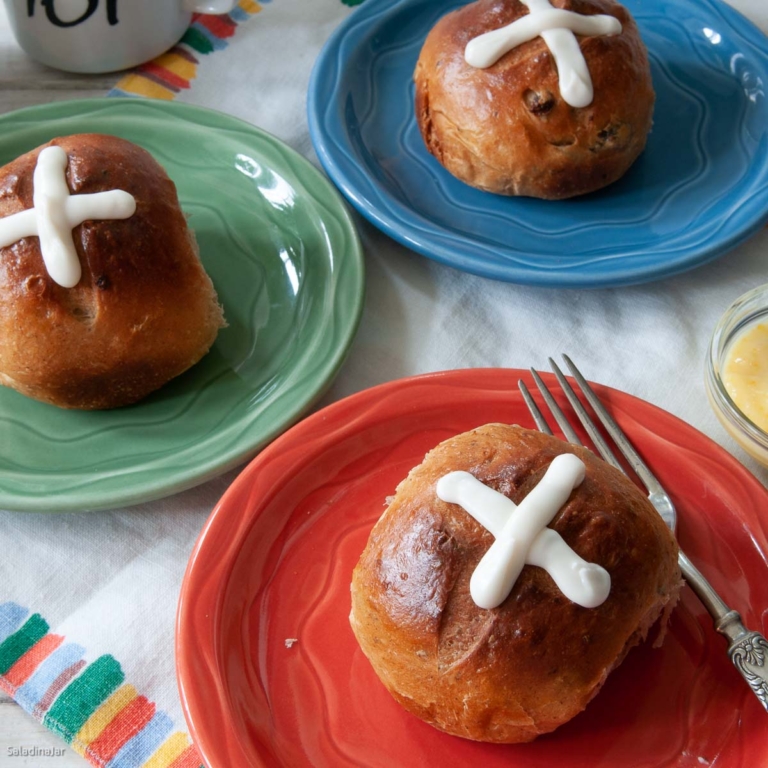 hot cross buns on orange, green and blue plates.