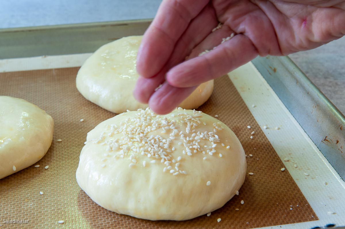 sprinkling the buns with sesame seeds.
