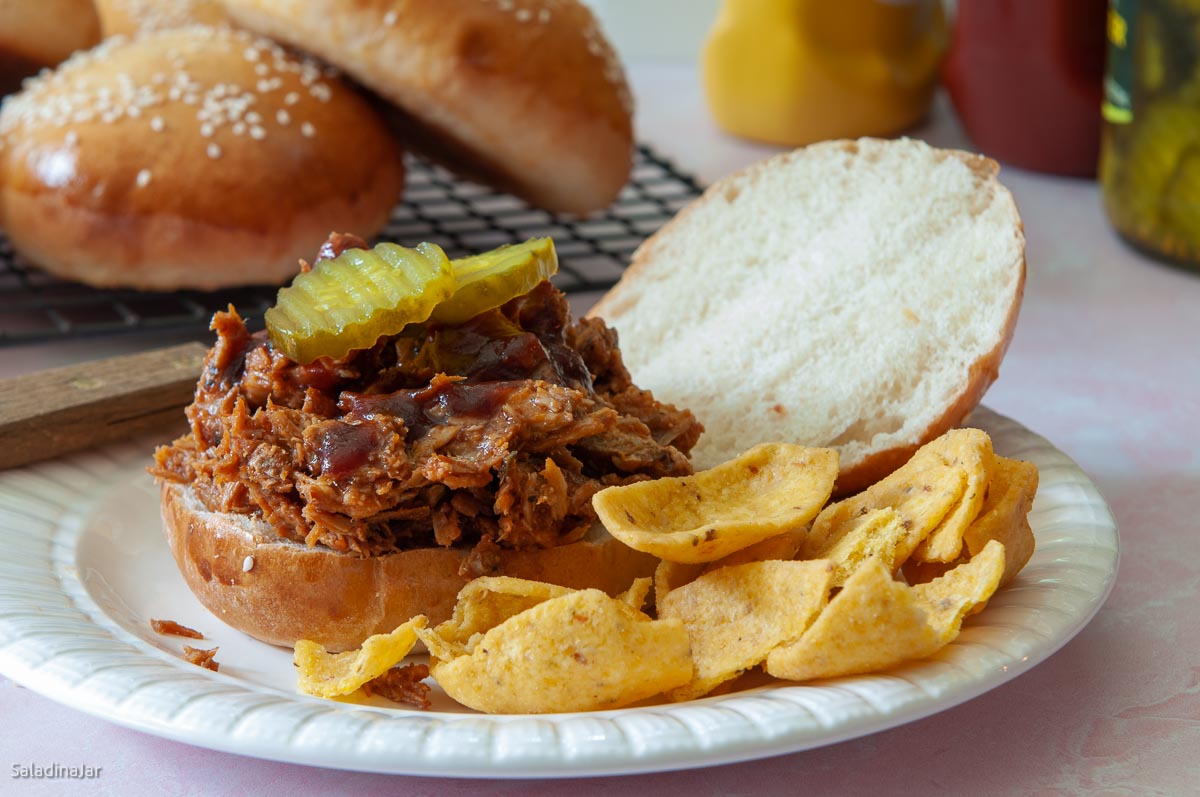 pulled pork sandwich made with a potato hamburger bun on a plate with Fritos