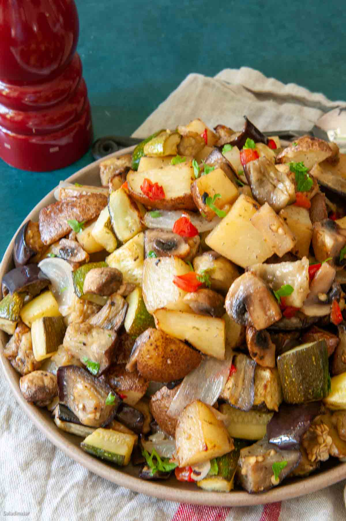 roasted eggplant and potatoes with zucchini and mushrooms garnished with parsley and red peppers