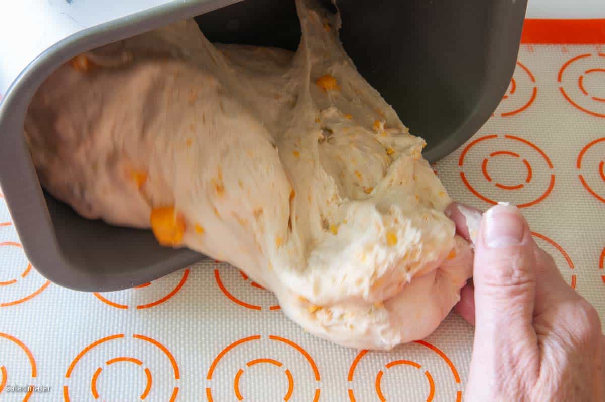 Pulling the dough out of the pan onto a lightly floured silicone baking sheet to prepare for shaping.