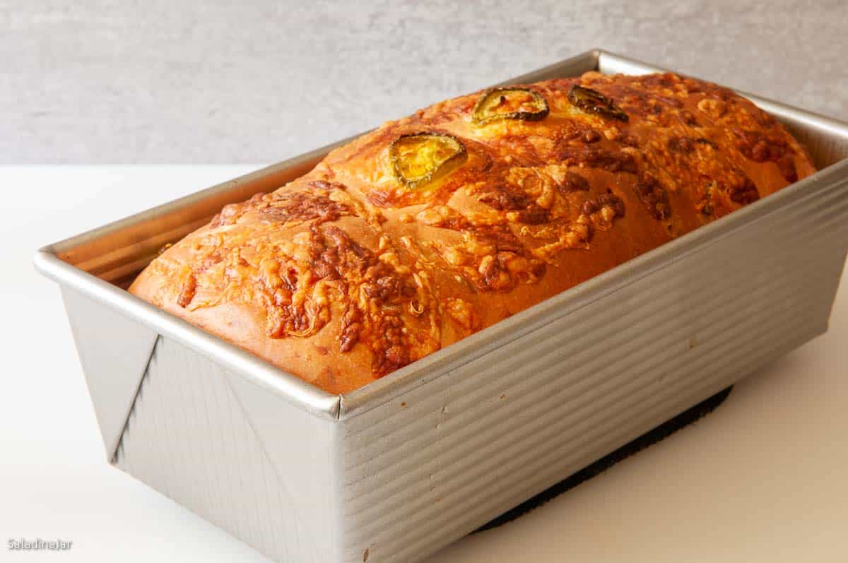 Baked cheese loaf with jalapeno slices and grated cheese on top.