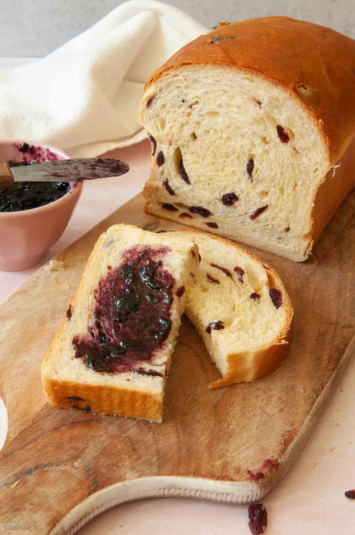 Sliced egg bread with dried fruit, one piece slathered with blackberry jelly.