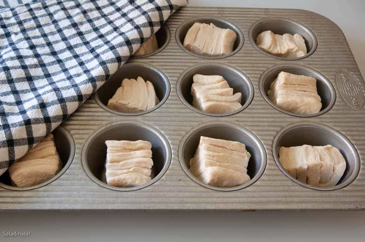 Placing the rolls into a muffin pan. Then cover.