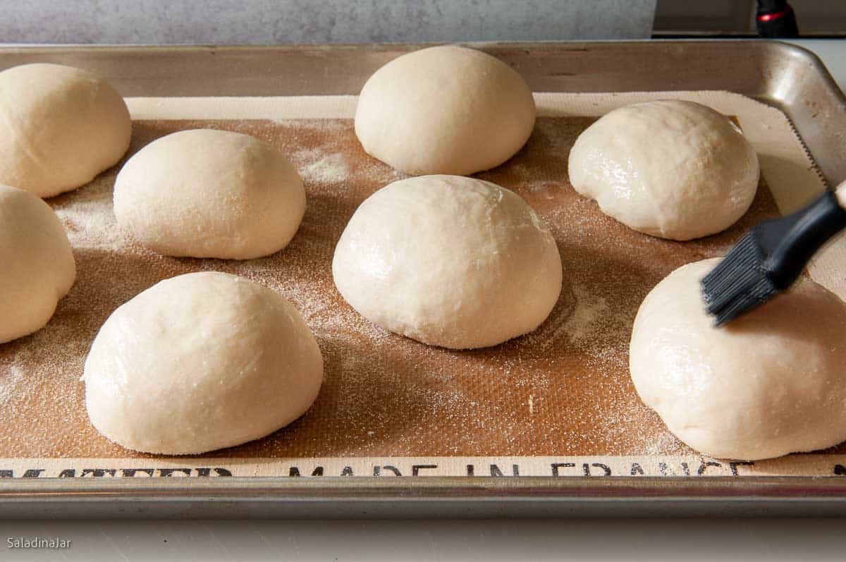 Brushing risen doughballs with cornstarch glaze.