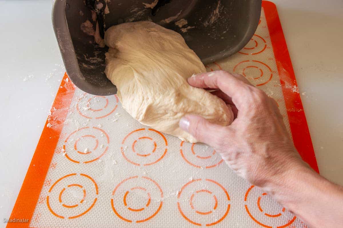pulling the dough out of a bread machine unto a floury surface (a silicone baking mat)
