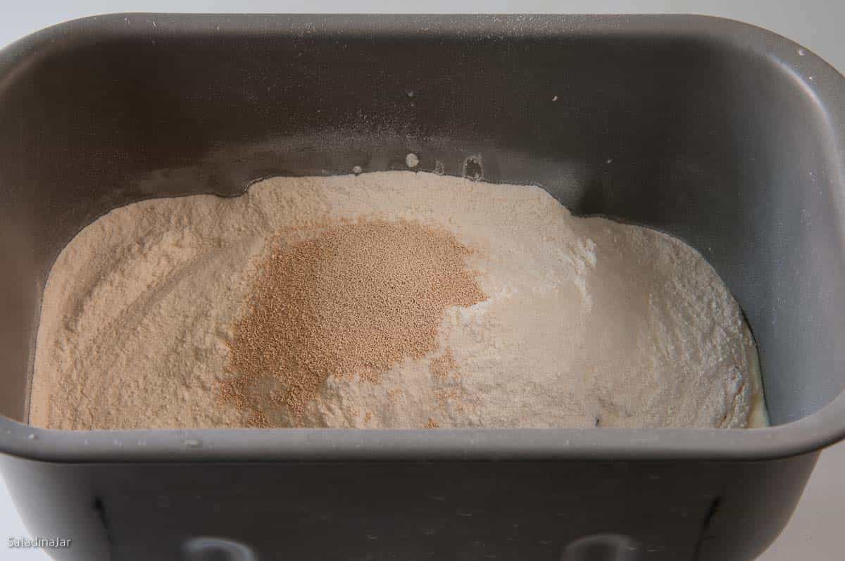 adding remaining dough ingredients to the bread machine pan.