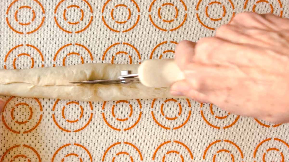 Cutting the dough in half with a pizza cutter.