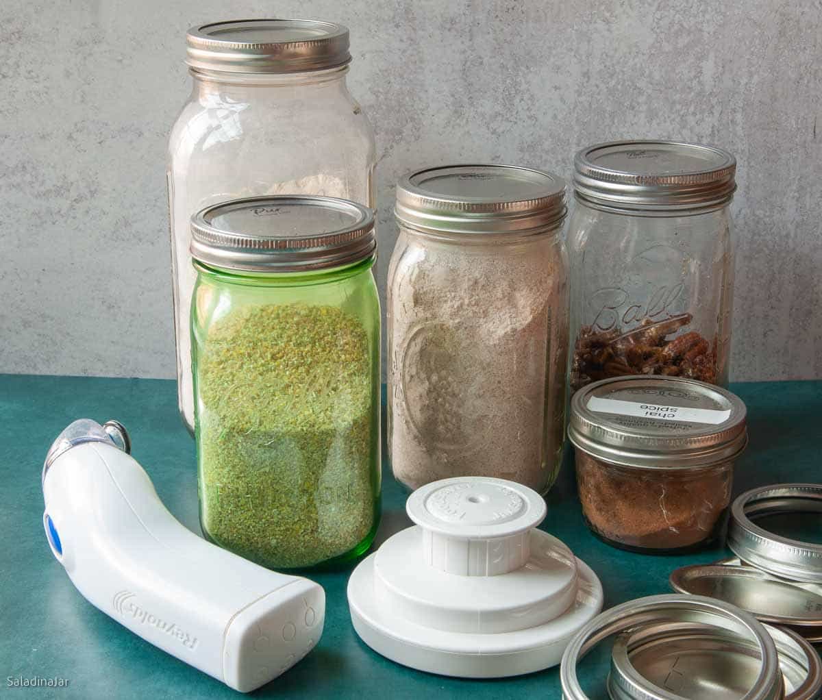 vacuum-sealed food in Mason jars pictured with a handheld vacuum sealer and widemouth sealer.