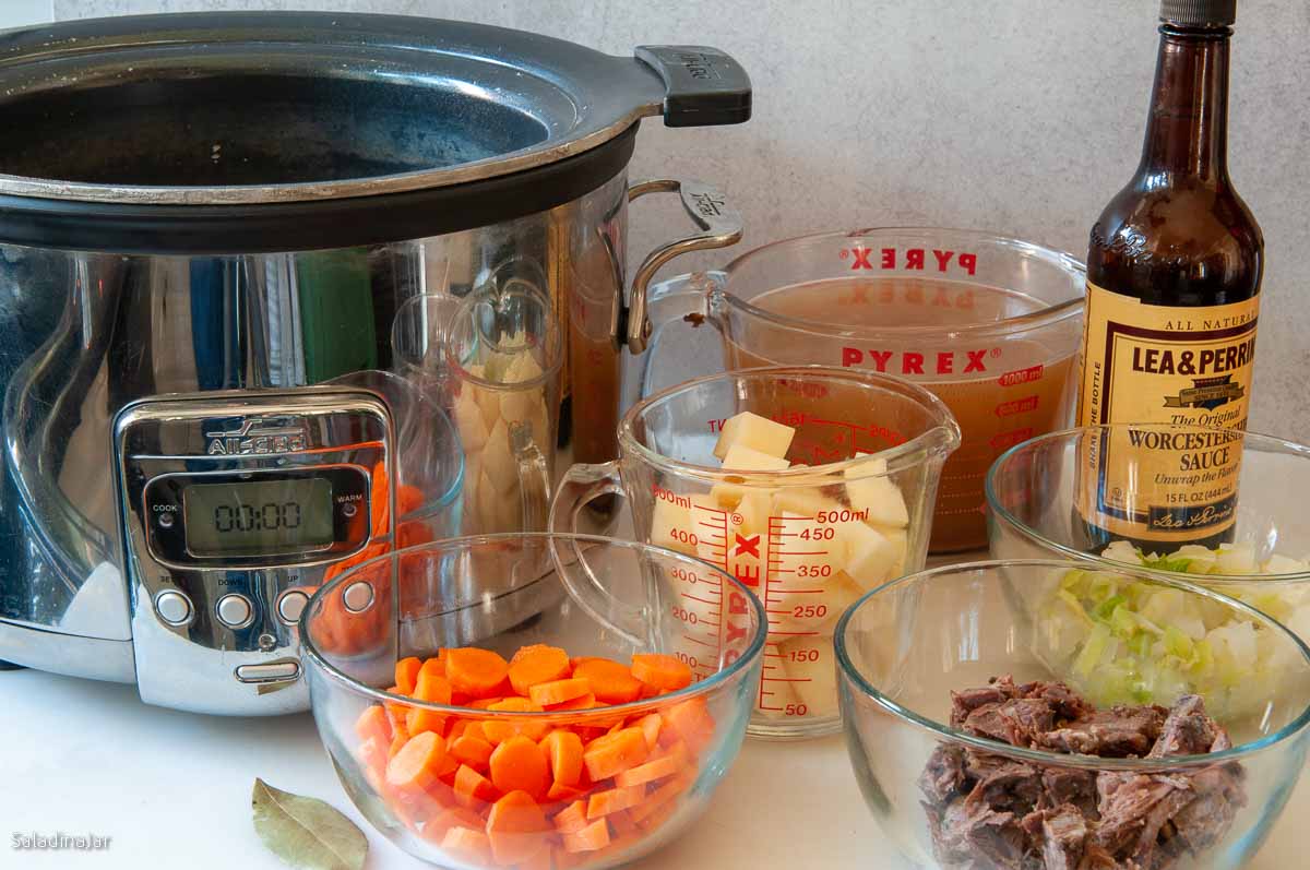 The first six ingredients for this soup are pictured sitting by a slow cooker.