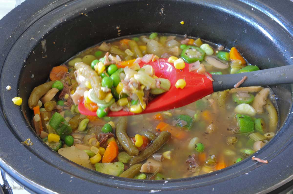 Finished soup in slow cooker container with a spoon showing all the vegetables.