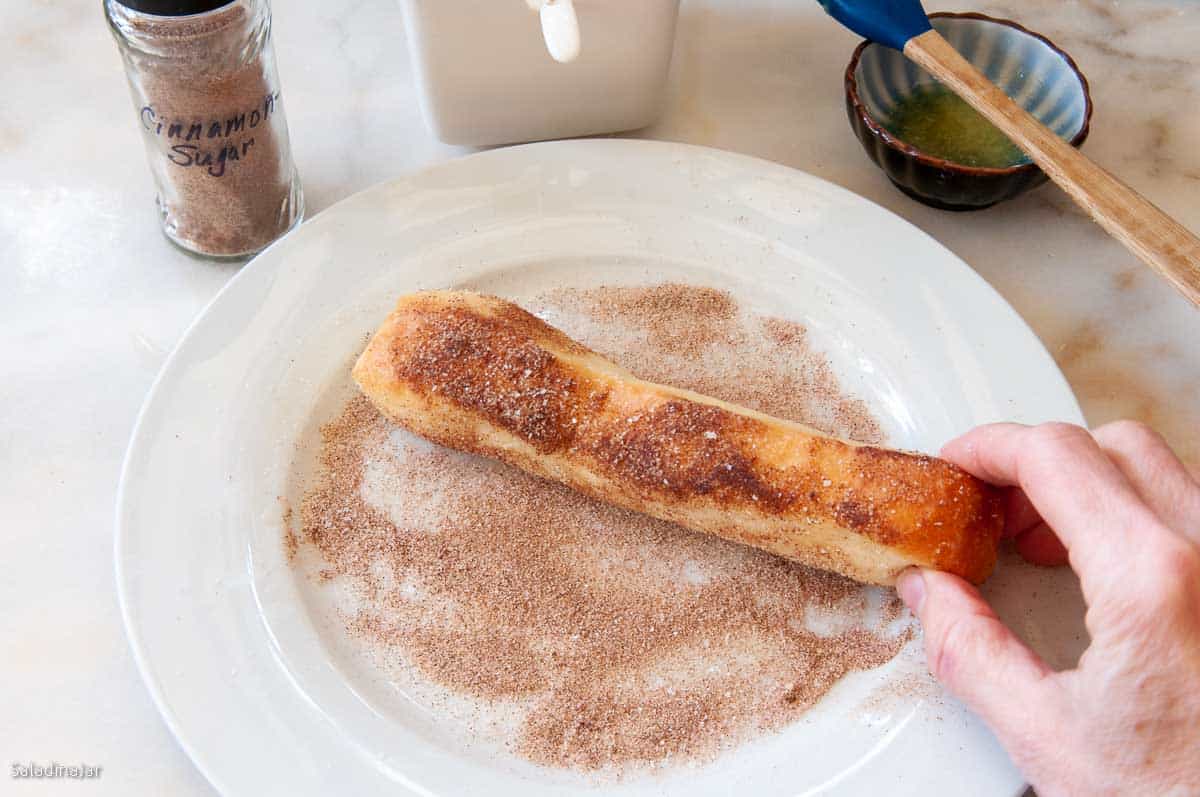 rolling bread stick in cinnamon and sugar on the plate.