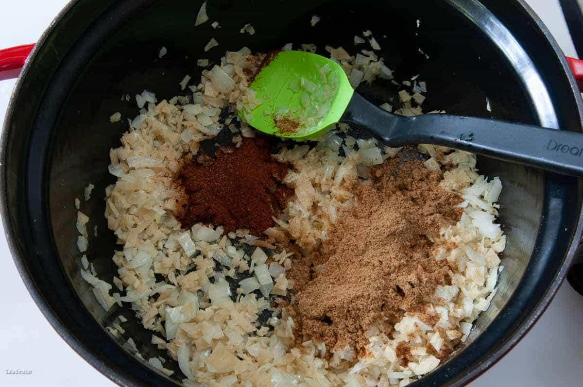 Cumin and chili powder added to the pot with a spoon.