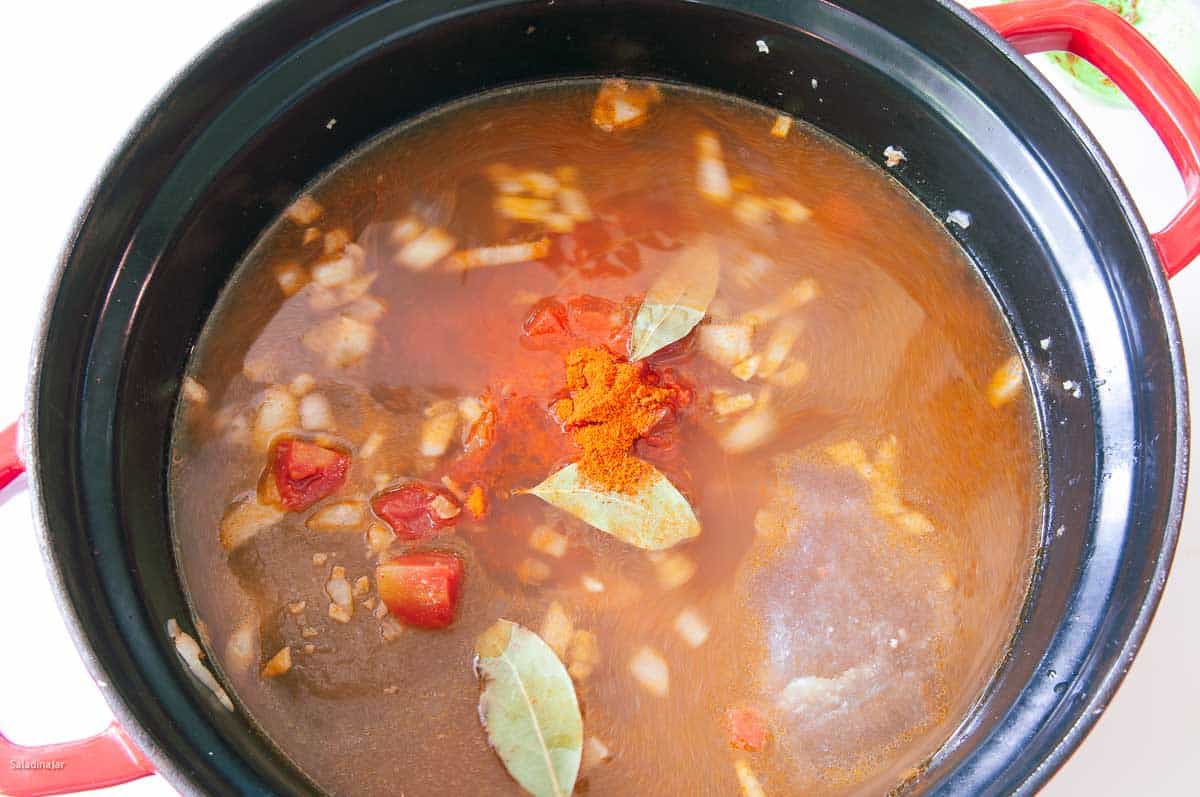 Adding the tomatoes, bay leaves, chicken broth, salt, and pepper.