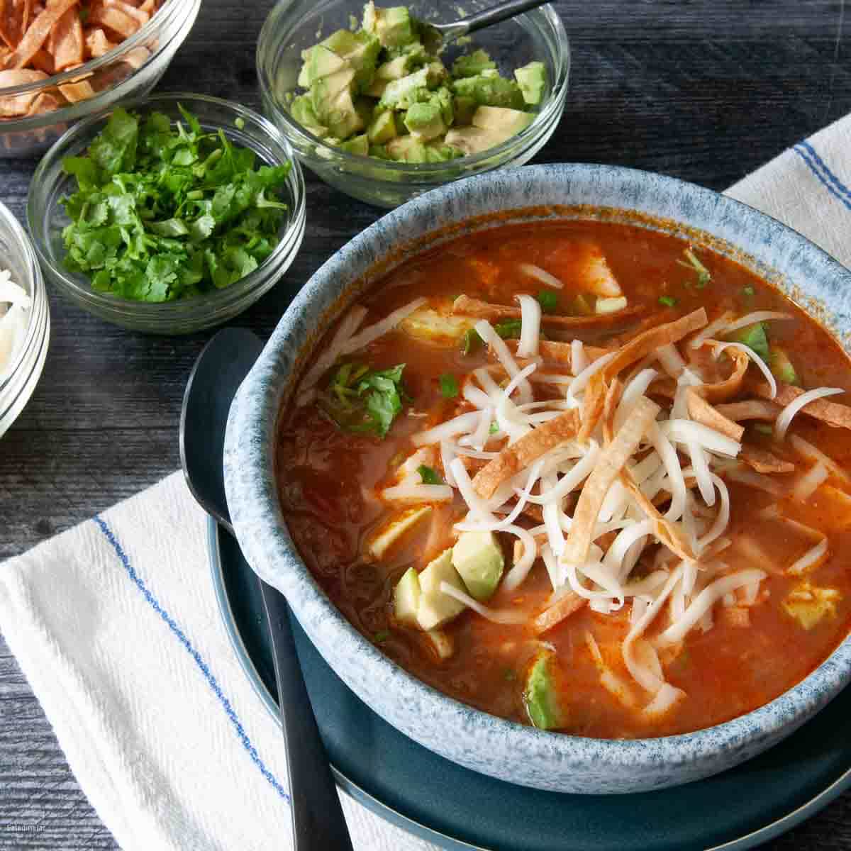 tortilla soup with spoon and surrounded with condiments.