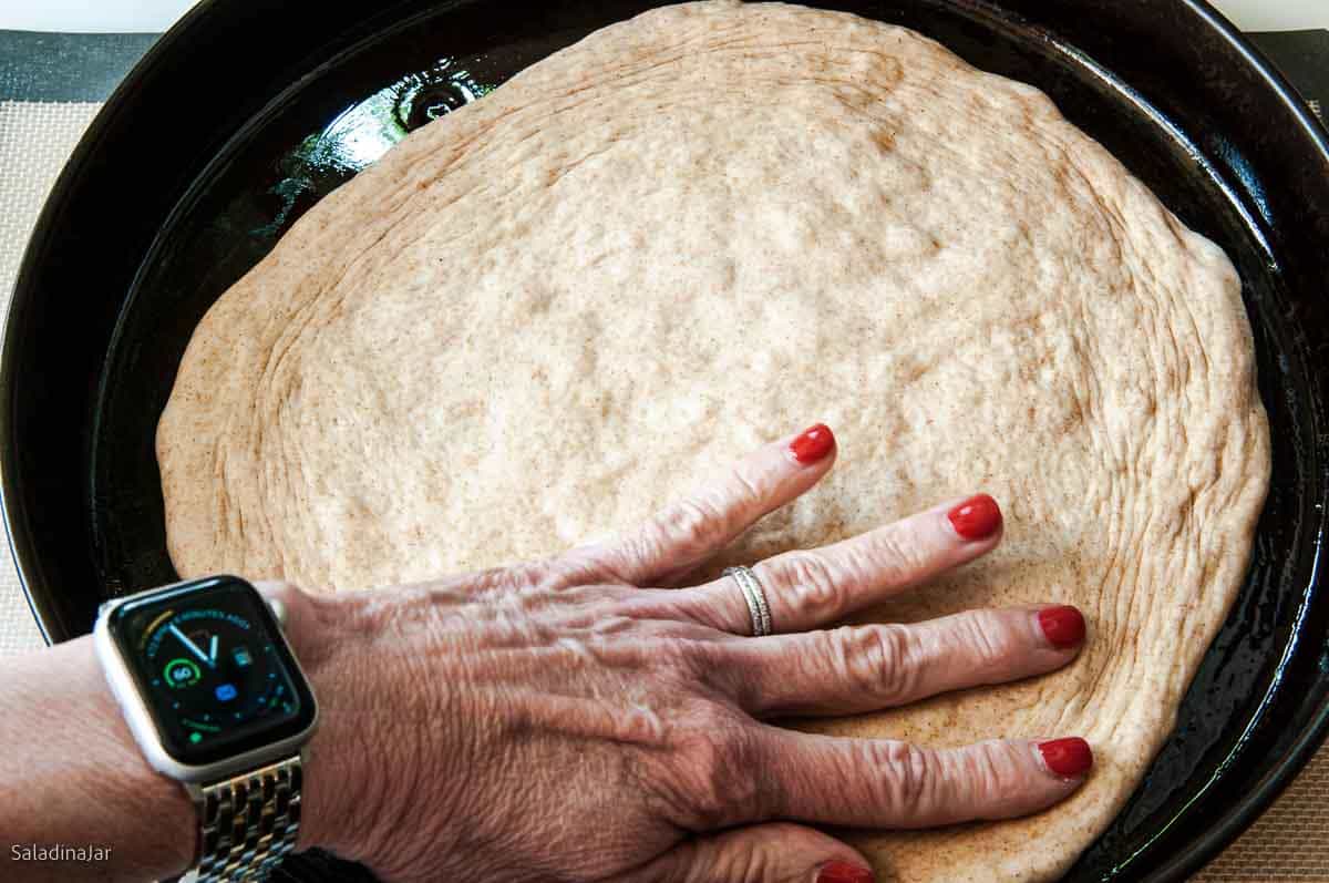 stretching dough with fingers inside an oiled pizza pan.