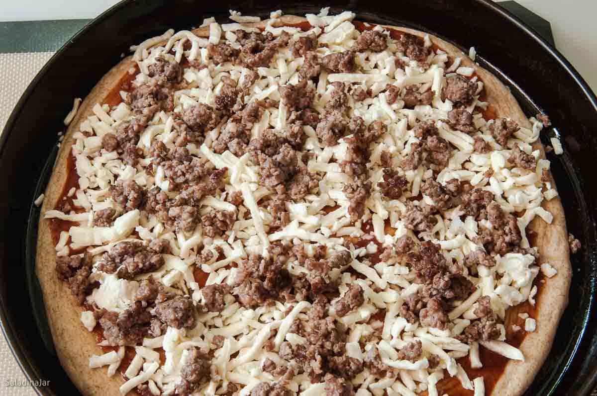 sausage topping is sprinkled over the top of the raw crust.