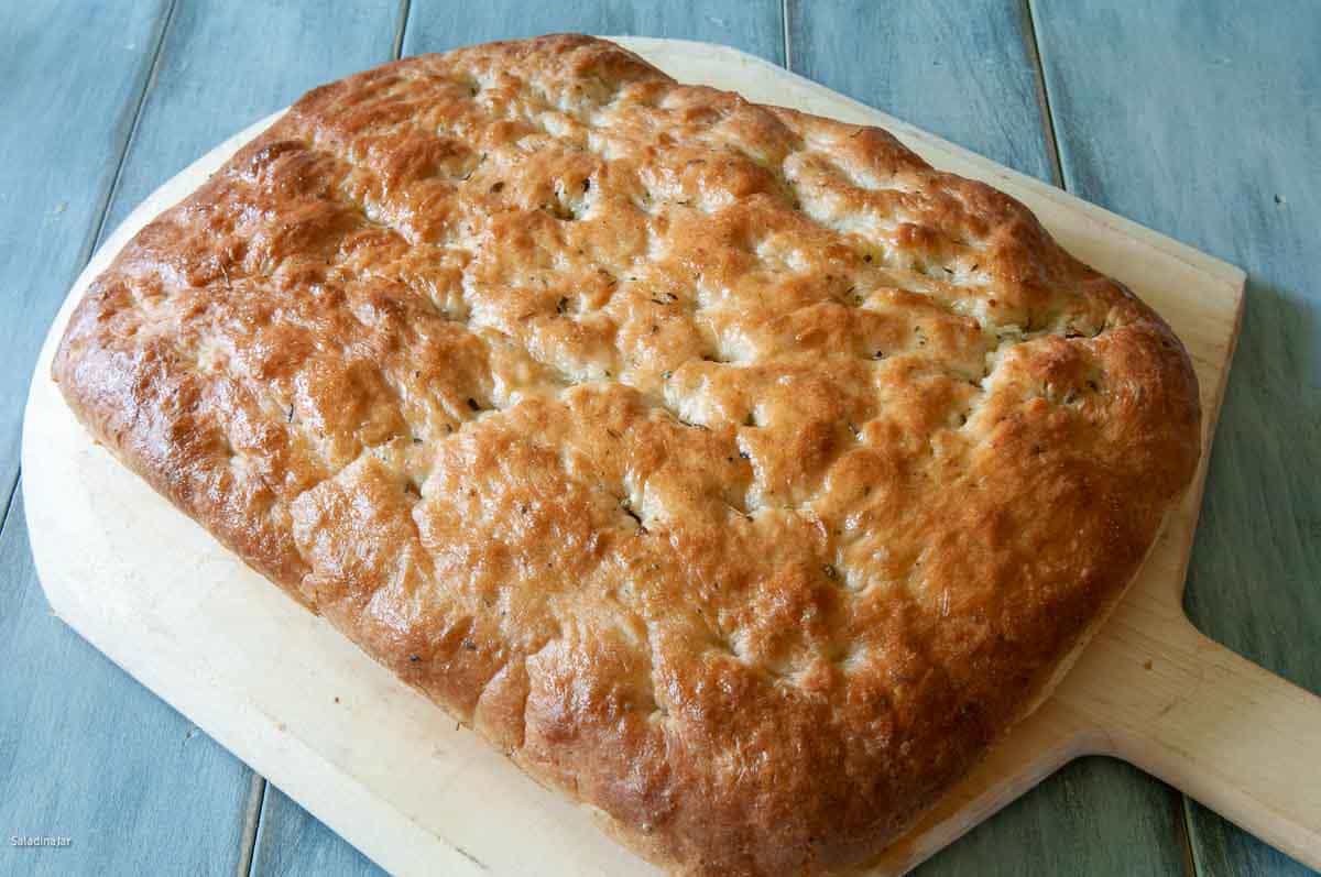 uncut focaccia bread cooling on a wooden board