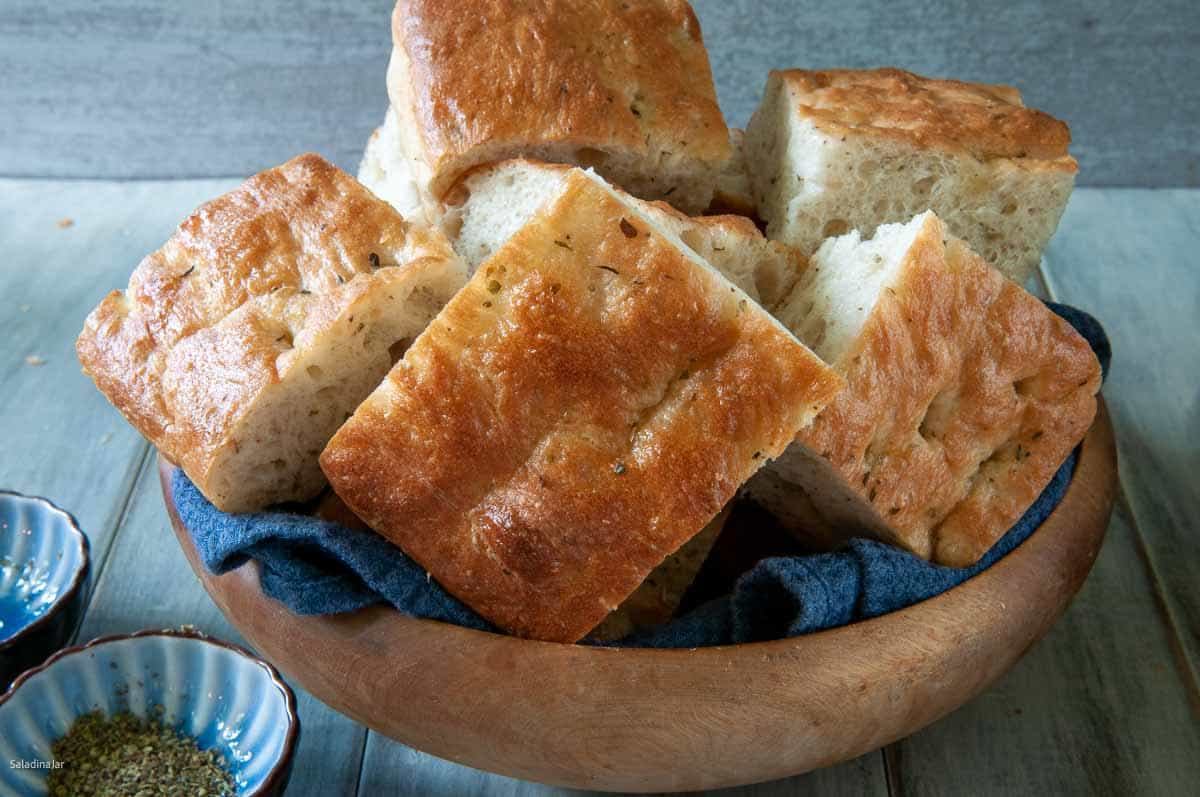 salt-free focaccia with Italian herbs cut in squares and stacked in a bowl.