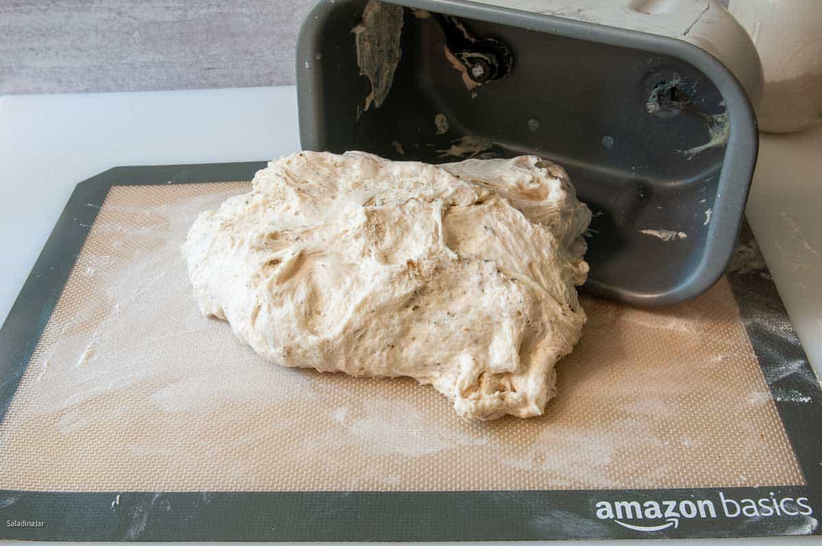 Pulling the dough out of the bread machine pan onto a lightly floured surface for shaping.