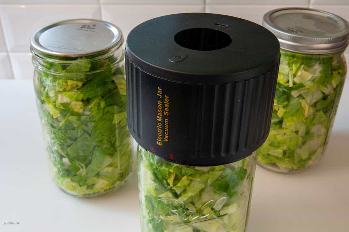 vacuum-sealed jars of chopped lettuce sitting next to an electric mason jar vacuum sealer.