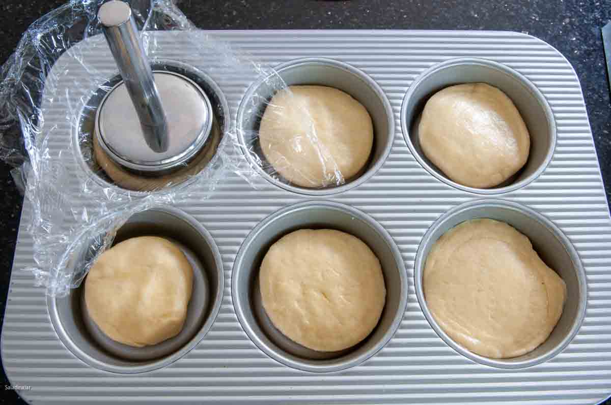 placing dough for hamburger buns into a bun pan and flattening with a burger pounder