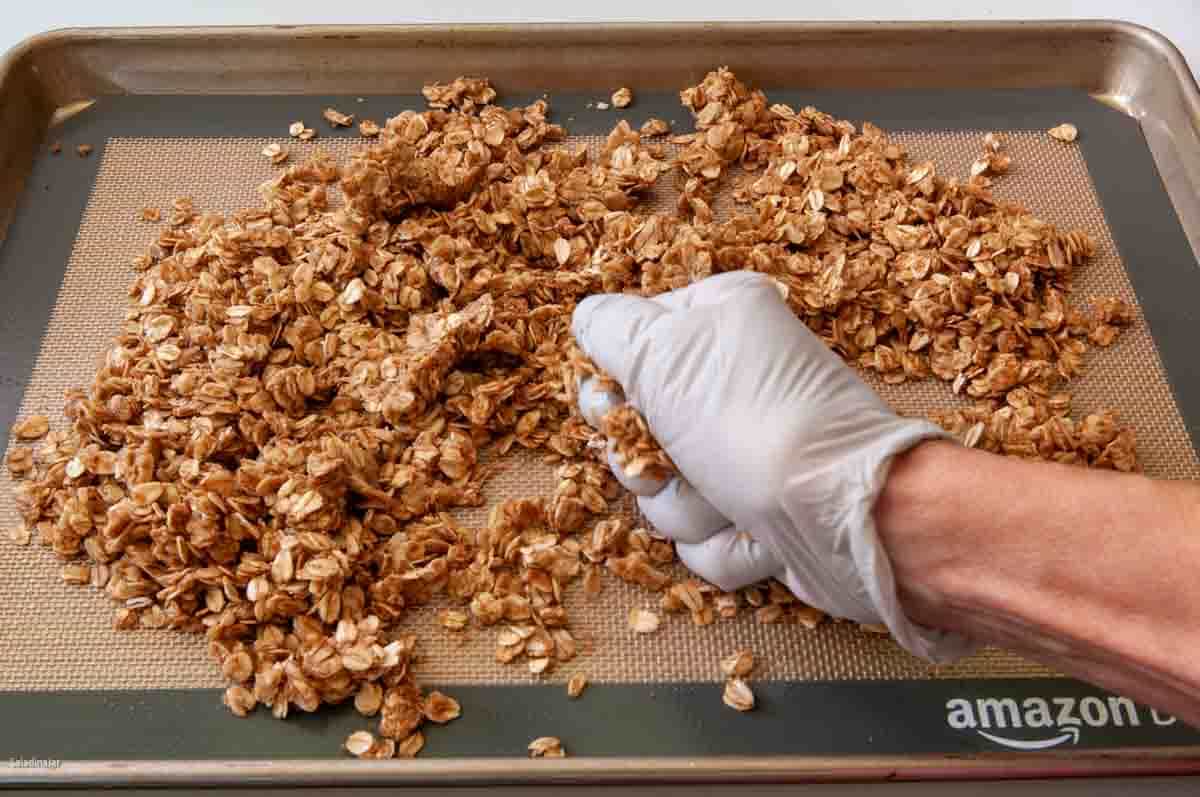 squeezing damp granola together with gloved hands to make clumps.