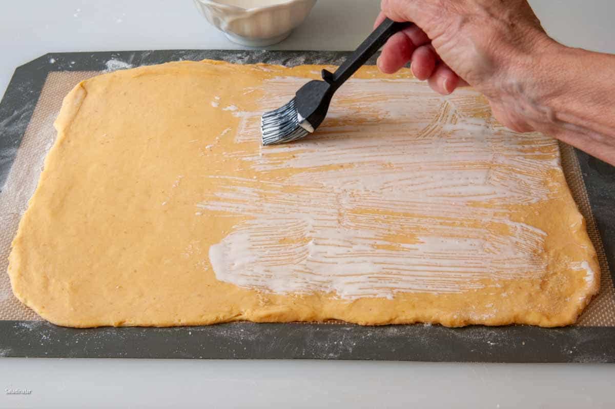 Brushing the surface of the dough with heavy cream or milk (acts as glue)
