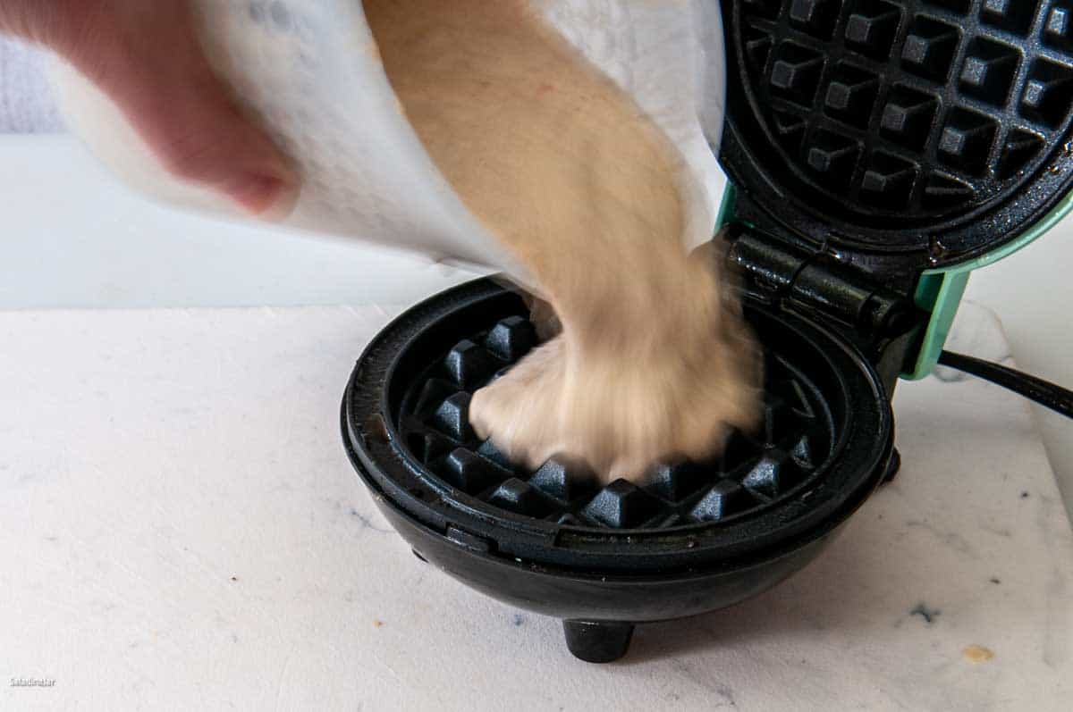 Pouring batter onto a waffle iron to make high-protein waffles.