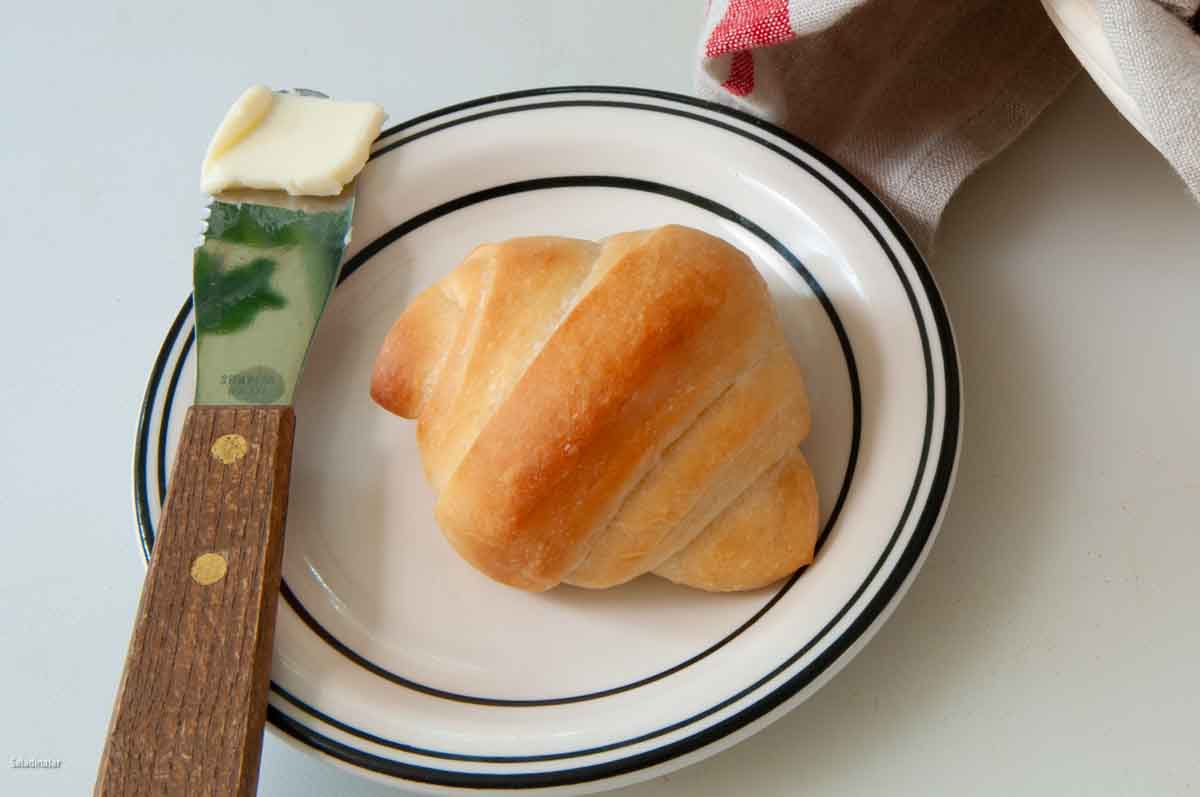a single butterhorn-shaped brown-and-serve roll with butter on the side.
