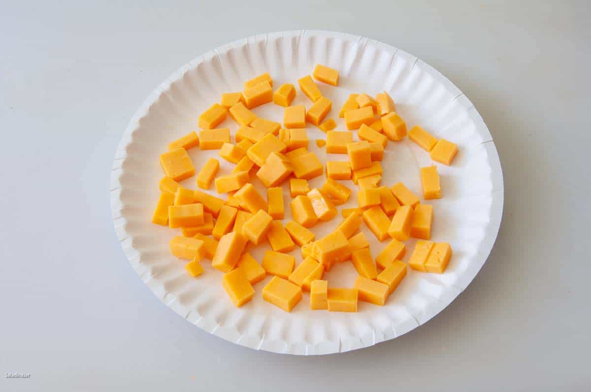 Small diced Cheddar cheese on a paper plate.